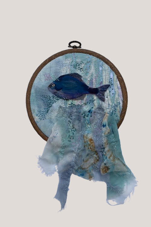 A dark blue watercolour fish stitched in an embroidery hoop, with tie-dyed cloth draping and hanging past the frame, hand-stitched for texture.